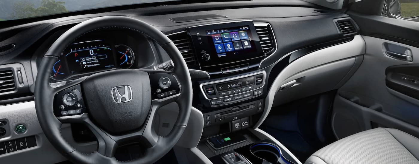 The grey interior of a 2022 Honda Pilot Elite shows the steering wheel and infotainment screen.