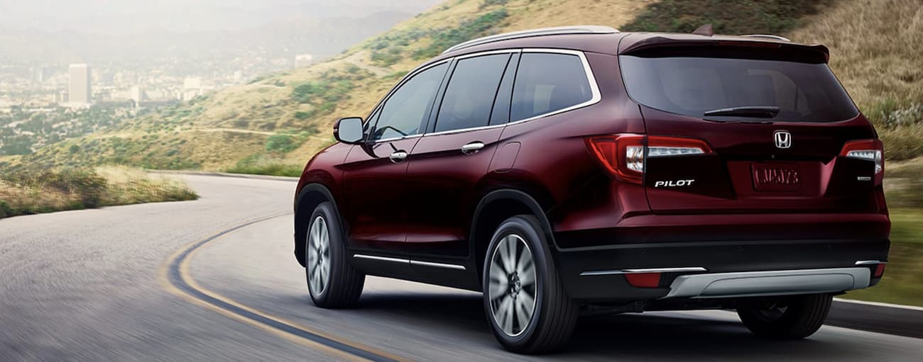 A maroon 2022 Honda Pilot Touring is shown from the rear driving on an open road.