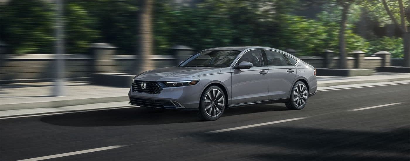 A grey 2023 Honda Accord Touring Hybrid is shown driving on a city street during a 2023 Honda Accord vs 2023 Nissan Altima comparison.