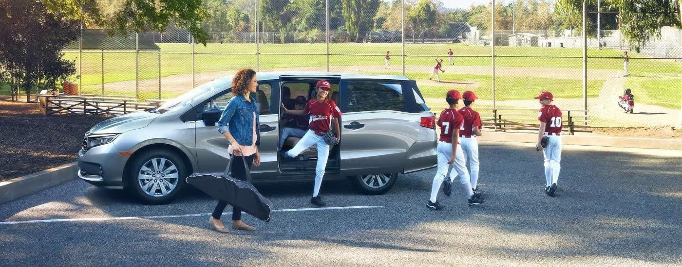 Children are shown near a silver 2024 Honda Odyssey Elite next to a baseball field.