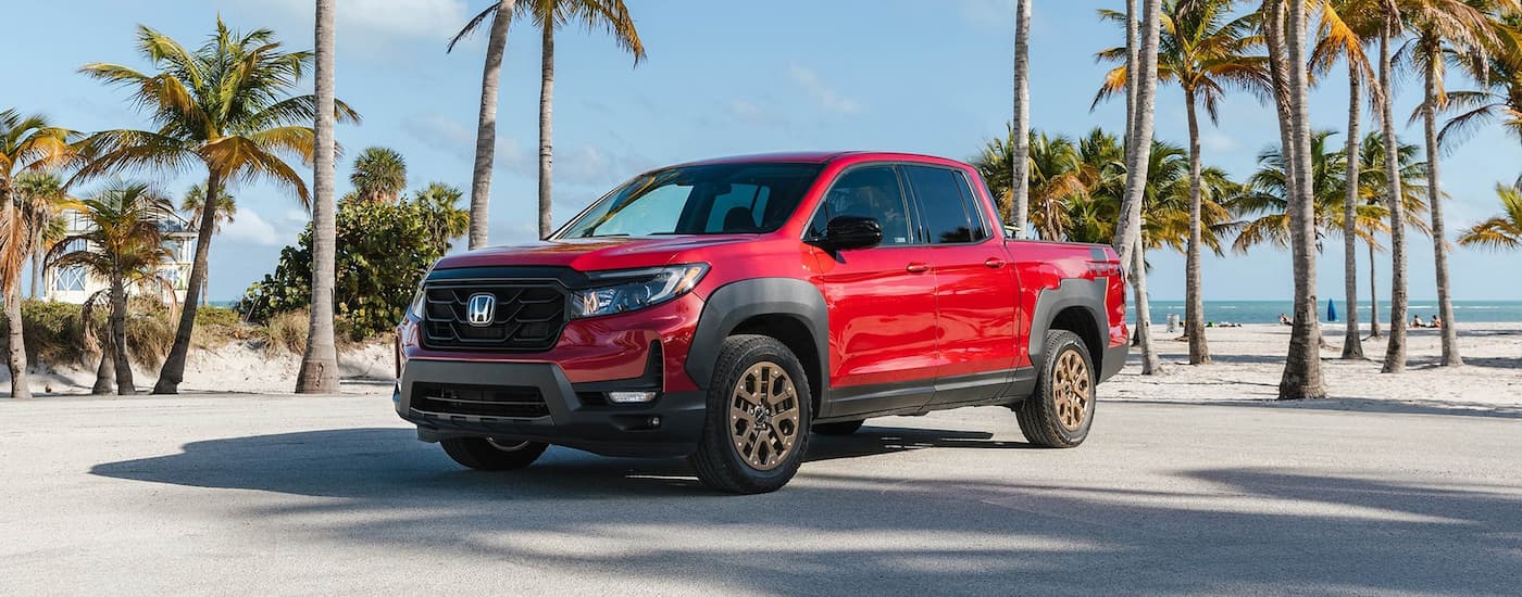 A red 2023 Honda Ridgeline Sport HPD Package is shown parked on a beach with palm trees.