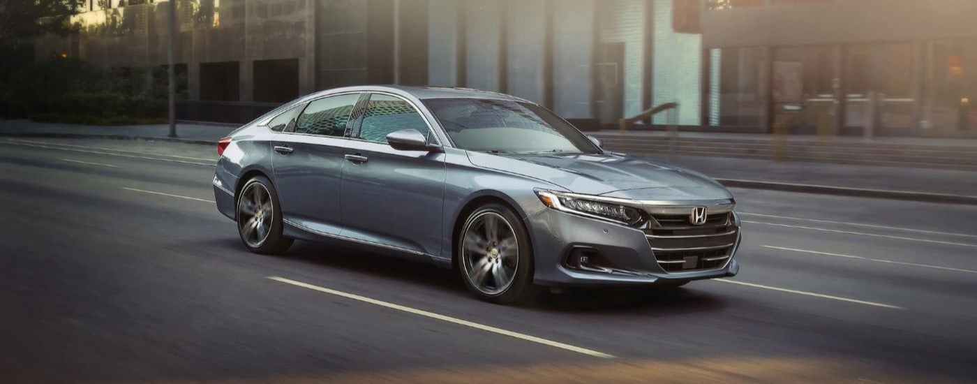 A grey 2021 Honda Accord Touring is shown driving on a city street after looking at used cars for sale.