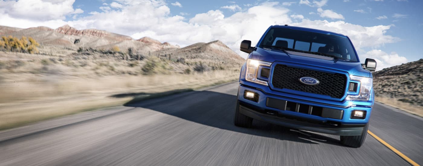 A blue 2018 Ford F-150 is shown from the front driving on an open road.