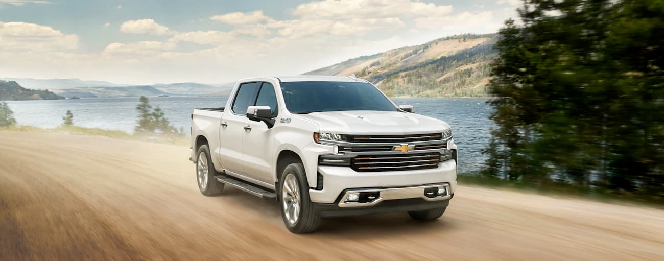 A white 2020 Chevy Silverado 1500 High Country is shown driving past a lake.