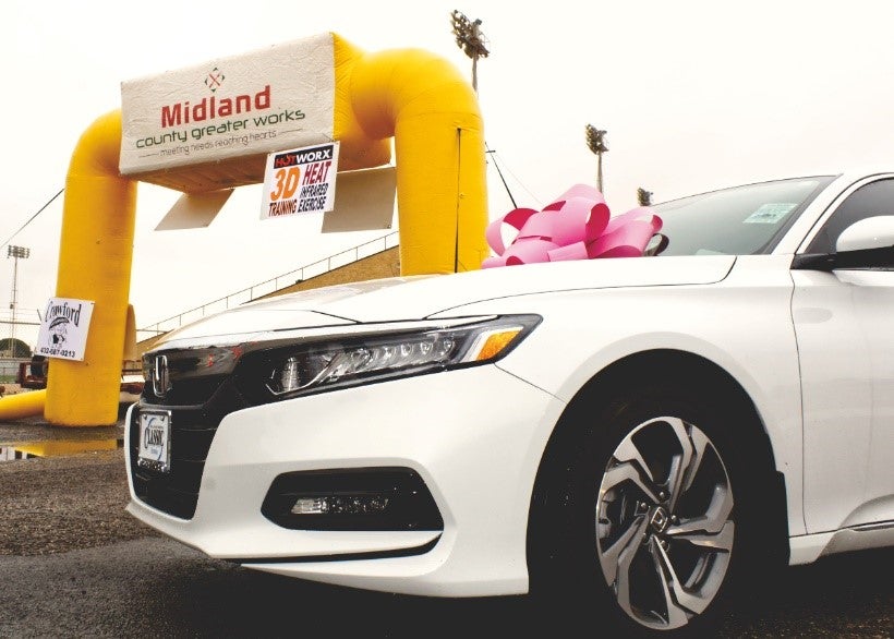 White Honda Sedan with a Pink Bow on it Parked in Front of a Midland County Greater Works Sign